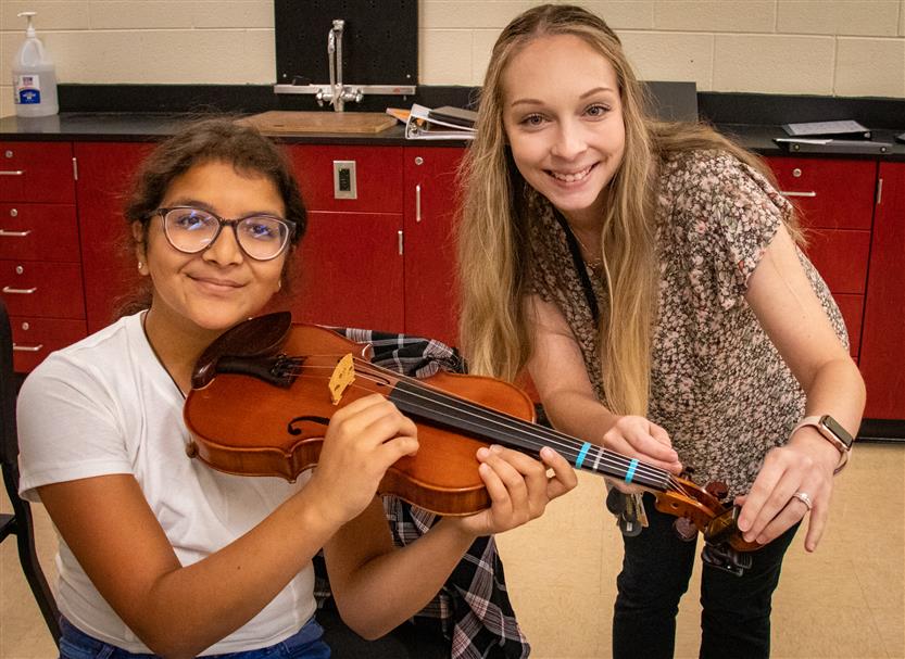 Two students smile while holding instruments